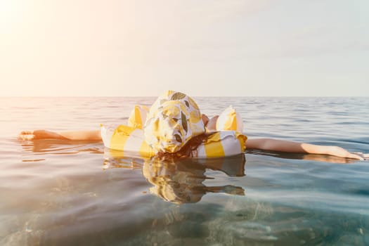 A person floats face down in a yellow and white patterned inflatable ring in a calm body of water.