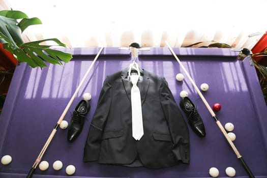 ..Black jacket, white tie, shoes, two billiard cues, billiard balls lie on the table.