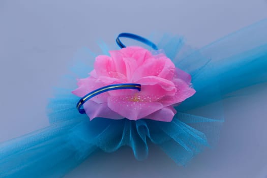 Decorative transparent blue ribbon with a bow and a pink artificial flower on a blue background. Wedding decor by car.