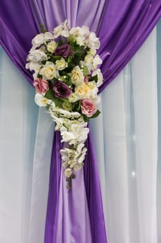 A colorful decorative bouquet hangs on a lilac and white curtain. Wedding decoration with flowers.Backdrop curtain decoration.