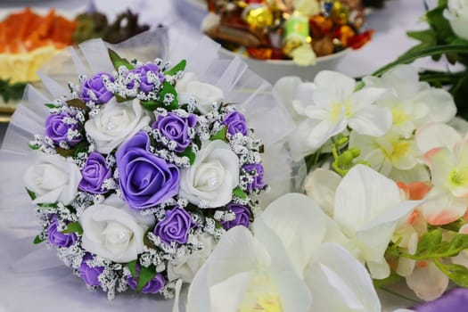 A bride's wedding bouquet with white and lilac flowers lies on a table with treats and other flowers close-up.