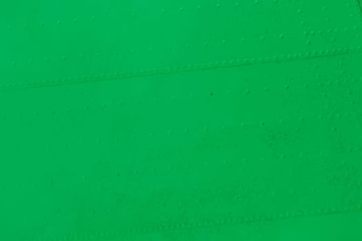 The surface of a metal wall with green rivets.Airplane fuselage painted green.