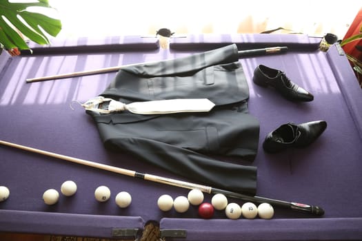 ..Black jacket, white tie, shoes, two billiard cues, billiard balls lie on the table.