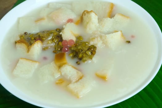 A bowl of Angsle, a traditional Indonesian dessert featuring green mung beans, bread cubes, and a creamy coconut milk-based broth, often sweetened with palm sugar and topped with rose syrup.