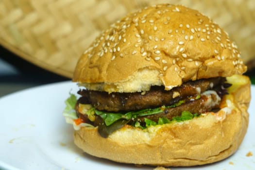 A delicious double patty hamburger with sesame seed bun, lettuce, and what appears to be a special sauce on a white plate.