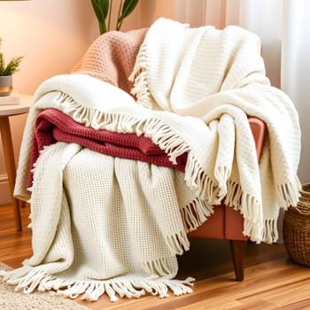 A collection of soft, textured blankets in cream and deep red are artistically draped over a comfortable armchair, creating a warm and inviting atmosphere in a cozy living space.
