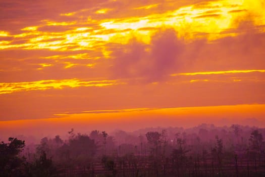 A breathtaking sunrise paints the sky in vibrant hues of orange and pink, casting a warm glow over a rural landscape dotted with trees and fields.