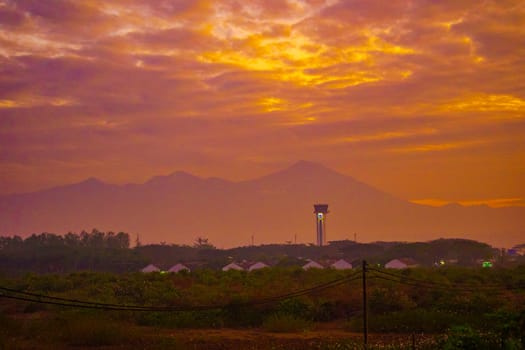 A breathtaking sunrise paints the sky in vibrant hues of orange and pink, casting a warm glow over a rural landscape dotted with trees and fields.