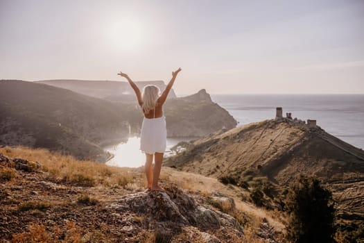 A woman is standing on a hill overlooking a body of water. She is wearing a white dress and she is happy