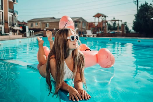 A woman is laying on a pool float in a pool. The pool is blue and the woman is wearing a white bikini