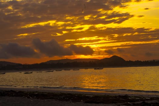 A breathtaking sunrise near Mandalika, Lombok, Indonesia paints the sky in fiery hues over a calm ocean, casting long shadows on the sandy beach and fishing boats.