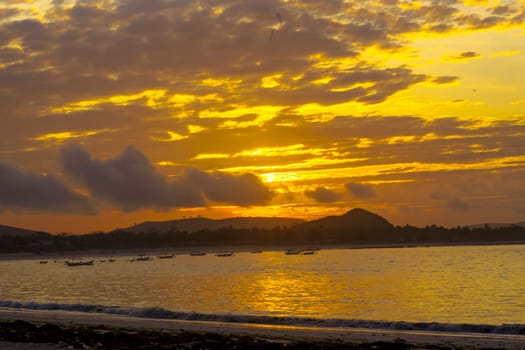 A breathtaking sunrise near Mandalika, Lombok, Indonesia paints the sky in fiery hues over a calm ocean, casting long shadows on the sandy beach and fishing boats.