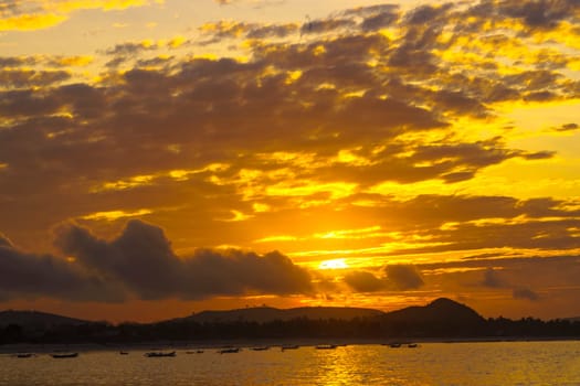 A breathtaking sunrise near Mandalika, Lombok, Indonesia paints the sky in fiery hues over a calm ocean, casting long shadows on the sandy beach and fishing boats.