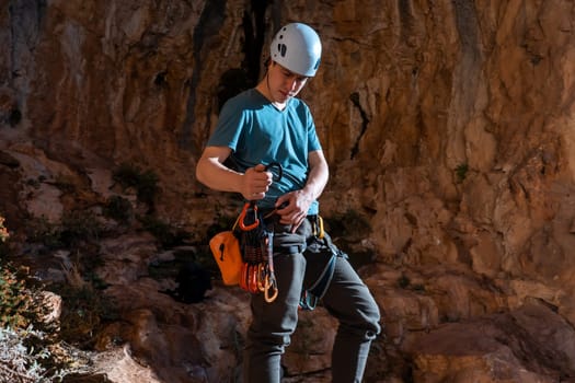 A man holds a carbine in his hand and fastens it to his climbing harness, the athlete is preparing for training on red rocks, is involved in active sports, rock climbing and mountaineering.