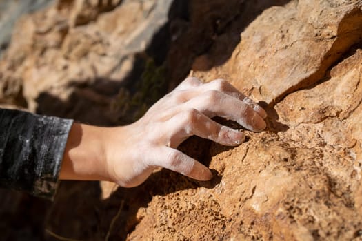 Hand of a rock climber in magnesia holding on to a rock, close-up view. The girl is engaged in active extreme sports, climbs up the mountain.