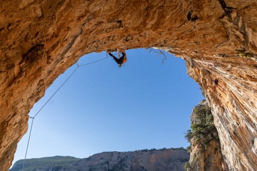 A man is professionally engaged in extreme sports, mountaineering and rock climbing, climbs the ceiling, the top of the cave against the blue sky on a sunny day in Twin Caves, Arcadia, Greece.