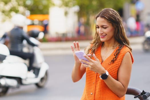 Latin woman scrolling the mobile in the street next to public rental bike service station