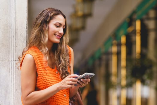 Latin blonde woman using phone smiling in the street