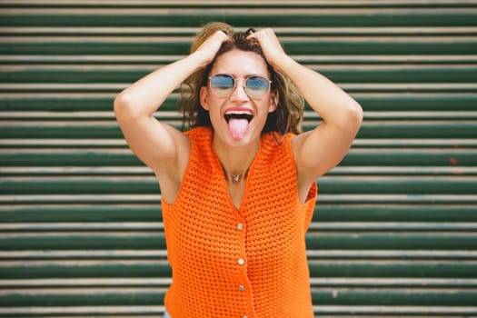 Urban portrait of a casual latin cool woman holing her hair and sticking the tongue out smiling