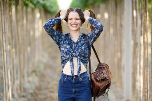 In a serene outdoor setting, surrounded by lush greenery, a joyful young woman in a colorful floral blouse playfully poses for the camera, radiating carefree happiness in that moment