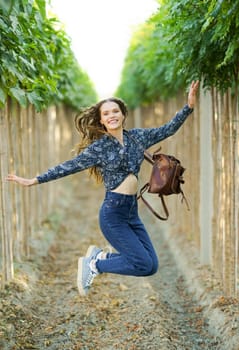 A radiant and cheerful young woman leaps joyfully along a vineyard path, exuding happiness and a sense of freedom while embracing the beauty of nature all around her under the sunny sky