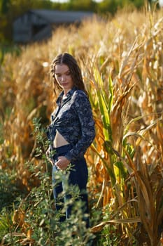 A stylish young woman confidently stands in a vast, golden cornfield, dressed in a trendy cropped shirt, gazing thoughtfully at her vibrant surroundings, embracing the beauty of nature