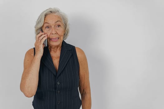 An elderly woman with beautiful gray hair is talking on her phone, expressing a sense of surprise or delight