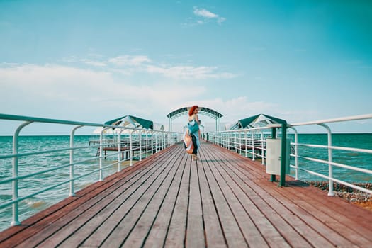 The resort pier comes alive with the presence of a woman sporting vibrant red hair, adorned in a summer dress, and carrying a backpack, enjoying a casual walk against the backdrop of the sea.