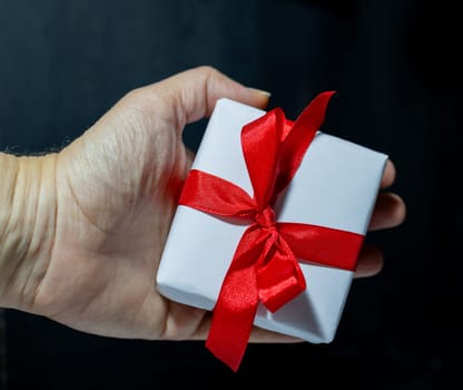 Christmas holidays concept.Woman holding a white gift box with red bow. Black background Real photo. Perfect for messages or promotions.