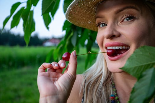 In the close-up shot, the woman's face and hands are the focal point. Her lips are painted and full, complementing her charming smile. With blue eyes sparkling, she exudes contentment, eager to indulge in the ripe cherries. In the background, a cherry tree branch and a blurred forest add to the tranquil ambiance. Holding a single red cherry between her teeth, the stem protruding, she displays her white teeth and tongue. The cherries, vibrant red and fully ripe, promise a burst of flavor. A straw hat adorns her head, completing the scene of a pleasant summer day. Her flirtatious smile adds a playful touch to the atmosphere. With the warmth of the sun embracing her, she embodies the joy of the season, relishing in the simple pleasure of savoring nature's bounty