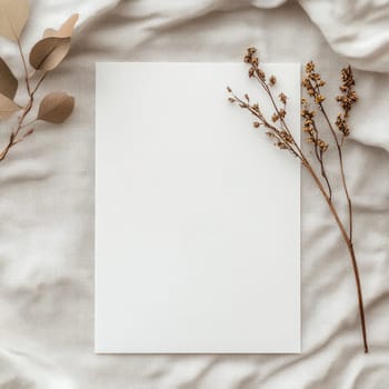 A piece of blank paper lies on a textured fabric backdrop surrounded by delicate dried flowers, creating an inviting space for writing or artistic projects.
