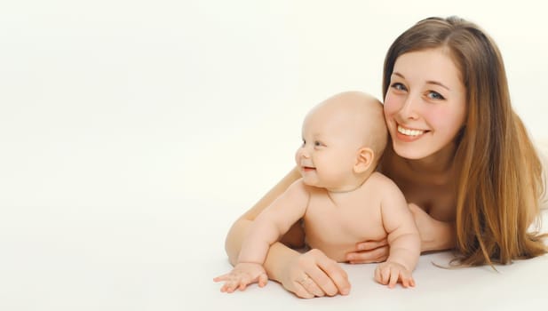 Portrait of happy smiling young mother playing with cute baby lying together on the floor on white studio background