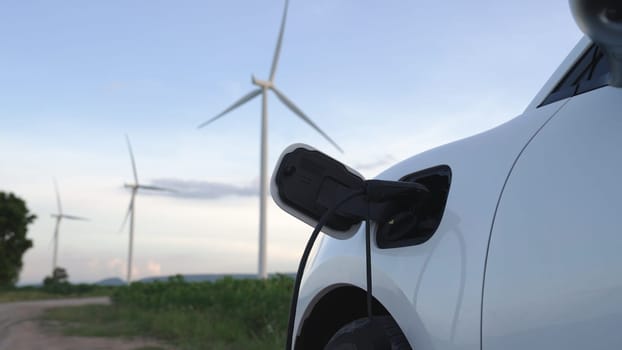 Progressive future energy infrastructure concept of electric vehicle being charged at charging station powered by green and renewable energy from a wind turbine in order to preserve the environment.