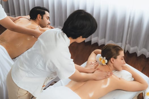 Caucasian couple customer enjoying relaxing anti-stress spa massage and pampering with beauty skin recreation leisure in day light ambient salon spa at luxury resort or hotel. Quiescent