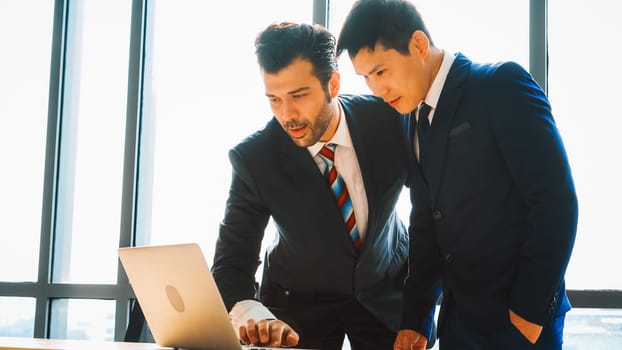 Two business people talk project strategy at office meeting room. Businessman discuss project planning with colleague at modern workplace while having conversation and advice on financial report. Jivy