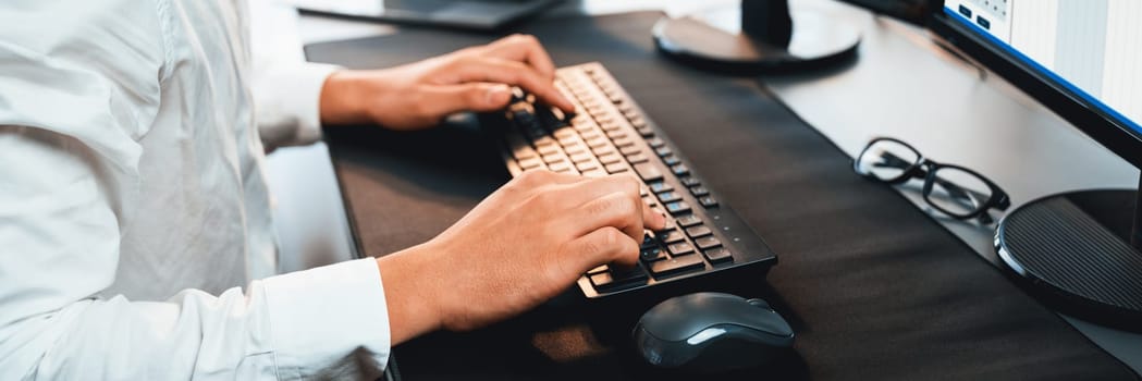 Office worker sitting on workspace desk, focused and engaged, using computer and typing on keyboard to input data ensure accurate data management in the modern workplace. Trailblazing