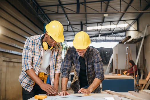 Craftsmen sketch of future project on blueprint paper in woodshop, Carpenter man wear helmet meeting planning a job together at carpentry workshop, team discuss, National Carpenters Day