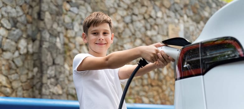 Little boy recharging eco-friendly electric car from EV charging station. EV car road trip travel concept for alternative transportation powered by clean renewable and sustainable energy. Perpetual