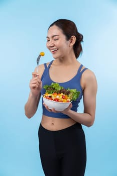 Young sporty Asian woman in sportswear holding salad bowl fill with vibrant of fruit and vegetable. Natural youthful and fit body lifestyle with balance nutrition on isolated background. Vigorous