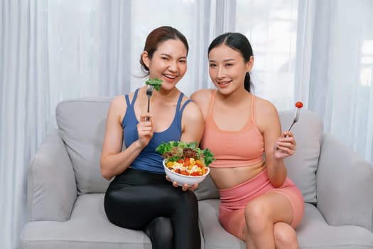 Young sporty Asian women in sportswear holding salad bowl together fill with vibrant of fruit and vegetable. Natural youthful and fit body lifestyle with balance nutrition and home exercise. Vigorous