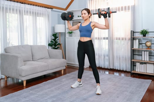 Vigorous energetic woman doing dumbbell weight lifting exercise at home. Young athletic asian woman strength and endurance training session as home workout routine.