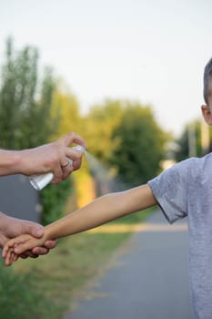 woman applies insect repellent to her son's hand in the park, close-up. Prevention of bites.