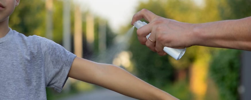 woman applies insect repellent to her son's hand in the park, close-up. Prevention of bites.