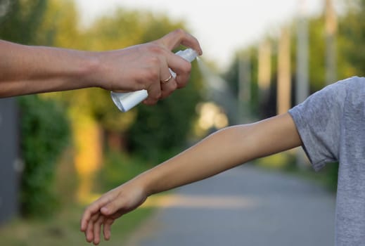 woman applies insect repellent to her son's hand in the park, close-up. Prevention of bites.