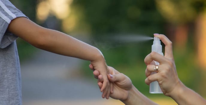 woman applies insect repellent to her son's hand in the park, close-up. Prevention of bites.