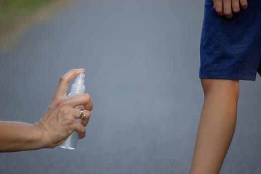 woman applies insect repellent to her son's hand in the park, close-up. Prevention of bites.