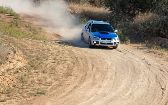 Sunny summer day. A sports hatchback takes a sharp turn on a dirt road and raises a cloud of dust