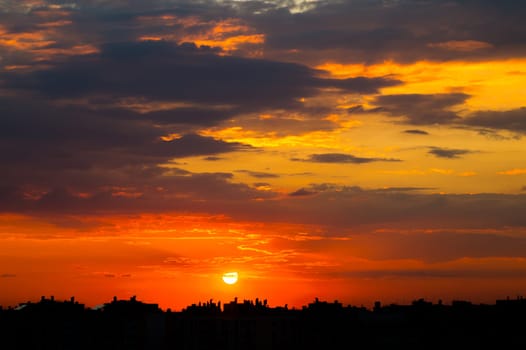 Cloudy sky over the roofs of the city. Sunset sun in the clouds above the silhouettes of buildings