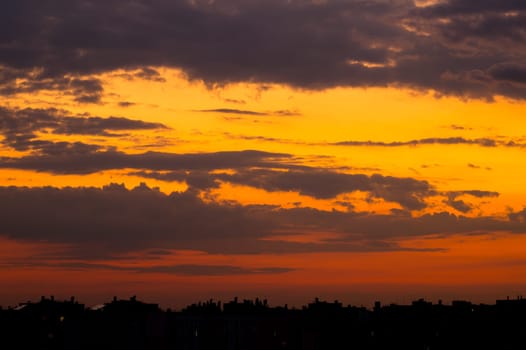 Cloudy skies over the city rooftops a few minutes after sunset. The last rays of light paint the clouds in shades of yellow and red