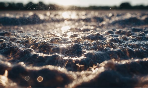 A close-up of water waves breaking and churning, creating foamy bubbles. The sun is shining brightly, creating a warm, golden glow on the water.